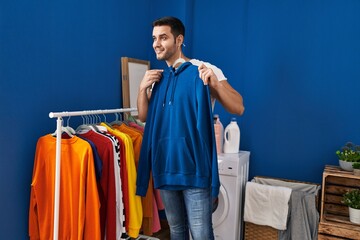 Young hispanic man putting clothes on clothes rack at laundry room