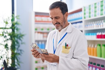 Middle age man pharmacist smiling confident counting dollars at pharmacy