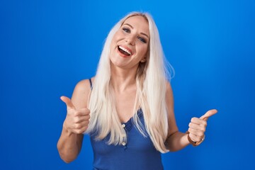 Fototapeta premium Caucasian woman standing over blue background success sign doing positive gesture with hand, thumbs up smiling and happy. cheerful expression and winner gesture.