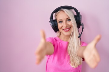 Caucasian woman listening to music using headphones looking at the camera smiling with open arms for hug. cheerful expression embracing happiness.