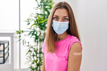 Young woman getting vaccine showing arm with band aid scared and amazed with open mouth for surprise, disbelief face