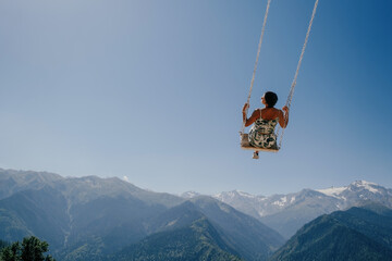 Fototapeta na wymiar Beautiful woman during summer day flying on swing in blue sky over a mountain landscape. Dream and travel concept