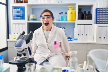 Hispanic girl with down syndrome working at scientist laboratory angry and mad screaming frustrated and furious, shouting with anger. rage and aggressive concept.