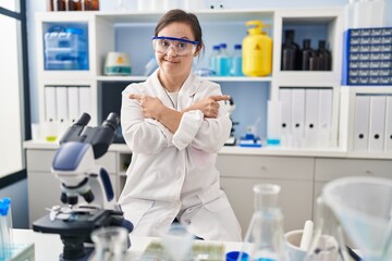Hispanic girl with down syndrome working at scientist laboratory pointing to both sides with fingers, different direction disagree