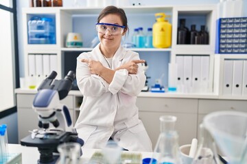 Fototapeta premium Hispanic girl with down syndrome working at scientist laboratory pointing to both sides with fingers, different direction disagree