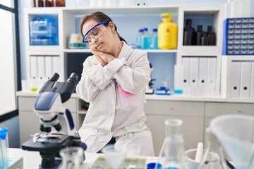 Hispanic girl with down syndrome working at scientist laboratory sleeping tired dreaming and posing with hands together while smiling with closed eyes.