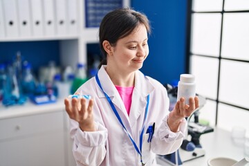 Young woman with down syndrome scientist smiling confident holding pills at laboratory