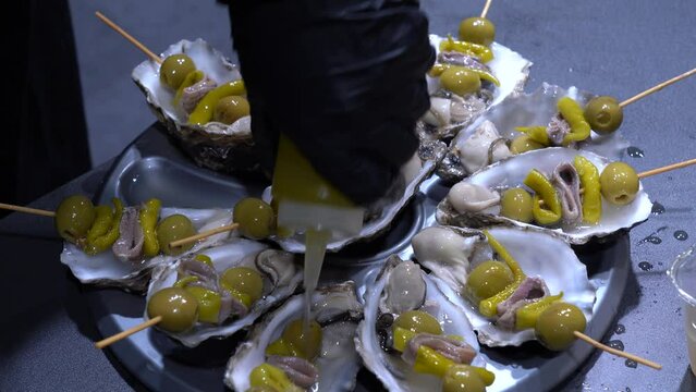Las manos de un cocinero ali&ntilde;ando unos aperitivos de una receta con ostras.