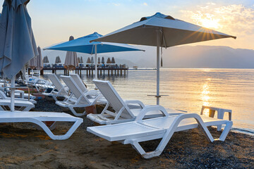 Beach umbrellas and sun loungers in the morning sun. Marmaris beach in the morning. Reflection of the sun in the sea. Turkey, summer, beach vacation.