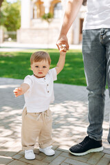 A little boy in a white shirt holds his parents' hands.