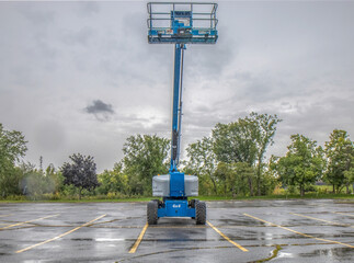Blue personnel basket lift truck  with hydraulic boom extended upward in an empty parking lot, light rain falling, nobody © Andre Savary