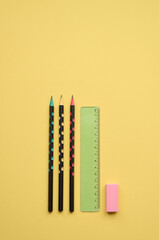 School supplies pencils, ruler and rubber isolated on yellow background, flatlay, minimal simple flat lay. Stationary stuff products for education, geometry tools. Back to school concept. Vertical