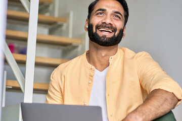 Happy smiling ethnic indian professional business man wearing earbud using laptop, laughing eastern businessman having virtual video call chat on computer elearning online education webinar from home.