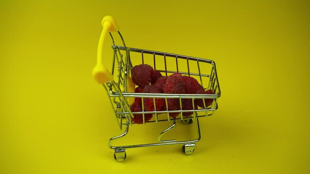 Shopping trolley overfilled with raspberries. Many berries fall into shopping cart
