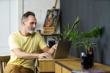 Portrait profile of handsome mature bearded man using laptop typing and checking data on screen. MIddle-aged manager working at home sitting at desk