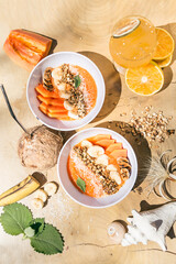 Vegan bowl. Papaya, banana, granola and coconut in a white bowl. Orange juice in a glass tumbler. All on a wooden table. Summer vibes