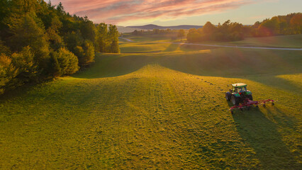 Fototapeta premium AERIAL Beautiful autumn morning light and rear view of tractor turning mowed hay