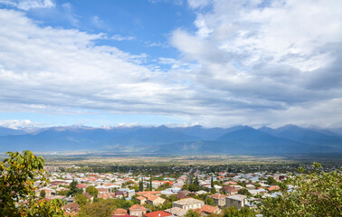 Fototapeta na wymiar Panoramic view of the Alazani Valley and the buildings of Telavi city with Caucasus mountain range in the distance, Kakheti region, Georgia