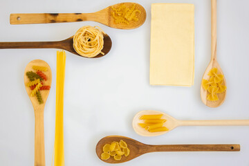 Different types of pasta in wooden spoons on a white background.