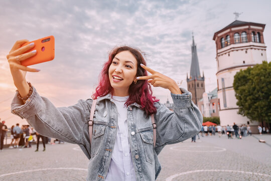 Happy girl travel blogger takes selfie pictures on her smartphone in the old city of Dusseldorf on the embankment and promenade of the Rhine River. Travel and German sightseeing locations