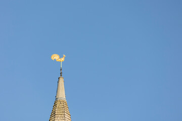 Weather vane, gold cockerel on a church spire set against a blue sky, copy space