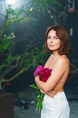 an attractive gentle woman with bare shoulders and arms with a peonies.