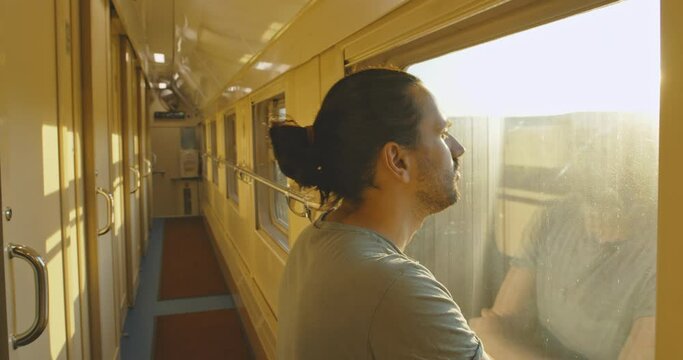 Young attractive tourist, looker out of the window of a moving train at sunset