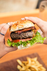Hands holding a burger, on a restaurant table. Delicious and nutritious food.