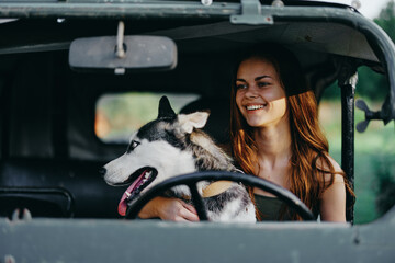 A woman driver of an old car travels in her car with a husky dog ​​in the evening at sunset and smiles. Lifestyle travel with an animal