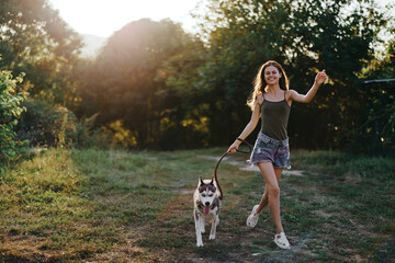 A woman runs with a dog in the forest during an evening walk in the forest at sunset in autumn. Lifestyle sports training with your beloved dog