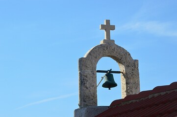 Simple bell tower with single smaller bell and stone cross on catholic church in Razanac, Croatia....