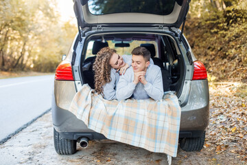Boy and girl are hugging in trunk of car. Autumn forest. Couple in love. Romantic date.