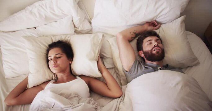 Noise, sleeping and snoring husband with a frustrated wife in bed, annoyed and uncomfortable. Young couple with problem in the bedroom, male suffering from sleep apnea, resulting in partner insomnia