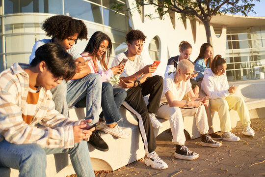 Group of young technology addicts using mobile smartphone outdoor. Multi ethnic millennial generation no social with new trends social media apps. Lens flare