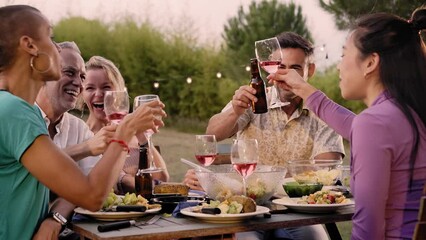 Group of friends toasting with wine having a barbecue in the backyard. Happy middle-aged people having fun at a picnic in the garden. 
