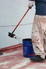 Construction worker applying 
black waterproofing material on roof dripping