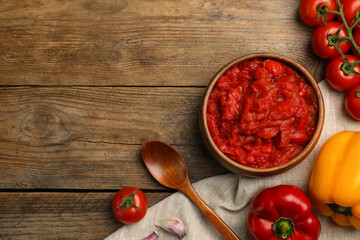 Delicious lecho in bowl and fresh ingredients on wooden table, flat lay. Space for text