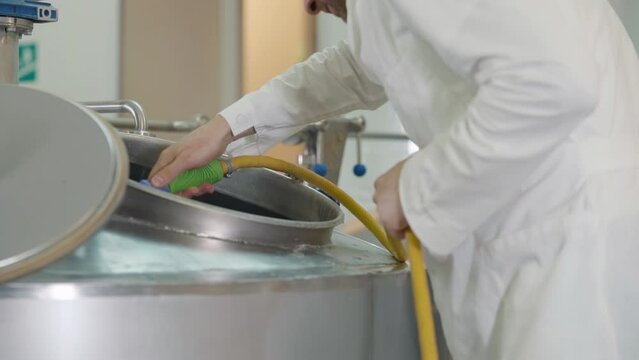 Worker cleaning industrial cistern used for alcoholic beverage manufacturing. Cleaning industrial cistern by spraying water from the hose. Cleaning industrial cistern under water pressure.