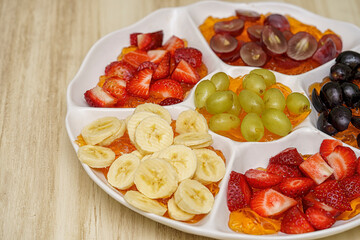 Tray with green, pink and black grapes, strawberries and bananas cut into pieces. flat-view