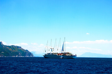 Majestic view in Amalfi coast at a huge colored ship with some sails and emergency vessels skimming the Tyrrhenian Sea with some imposing mountain cliffs in the background under a sunny sky