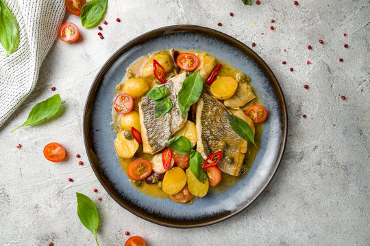 Dorado on grill with mini potatoes and artichokes on plate on grey table top view