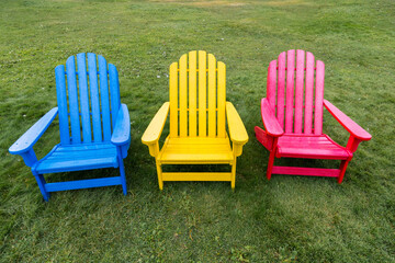 Colorful blue, yellow, and red Adirondack chairs on a green lawn
