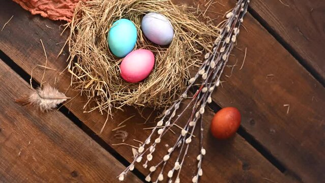 Easter is still life. Painted colorful chicken eggs in a hay nest, willow branches and fabric on a wooden table. Gyration. High quality 4k footage
