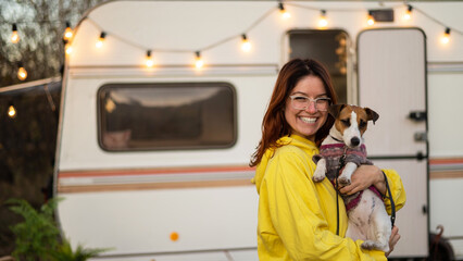 Red-haired Caucasian woman hugs a dog and lives in a motor home. Travel by trailer. - obrazy, fototapety, plakaty