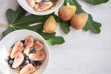 Top view of Fresh fig. blueberries and cereal in white ceramic bowl on white wooden background. copy space.