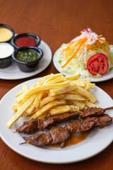 anticuchos with papas, accompanied by salad, and all their creams