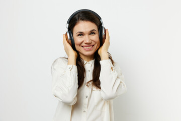 an emotional, beautiful, pleasant woman stands in a white shirt listening to music and holding headphones with her hands, smiling pleasantly with pleasure.