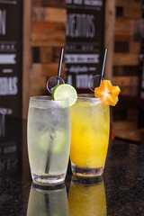 Low angle close up of ice cold modern gourmet craft cocktail of gin and tonic soda garnished by lemon slice and rosemary sprig sprinkled bar background - Imagen