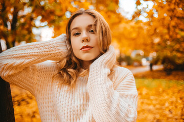 Photo portrait of a girl in a white sweater, the blonde holds the neck of the sweater and looks at...