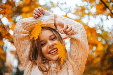 Photo portrait of a girl in a white sweater, the blonde holds a leaf in her hand. Pretty woman in the park in autumn laughs, joy, smile. Autumn fashion and style.